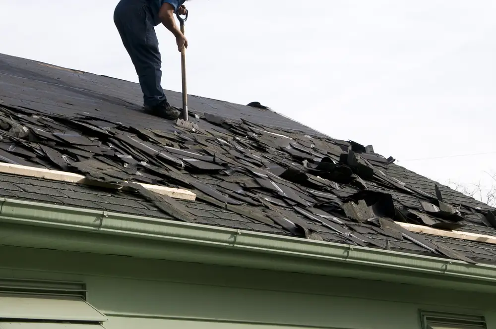 A Northland Roofing contractor clears debris as part of a roof replacement during a re-roofing job.